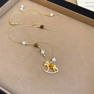 Detailansicht eines goldenen Schaukelpferd-Anhängers mit Tigerauge und Perlenkette