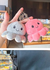 Pink and gray reversible plush octopus keychains hanging on a black bag strap
