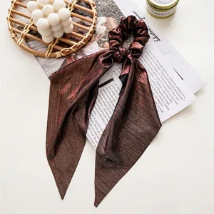 Detail of metallic pleated hair scrunchie with long ribbons in bronze finish