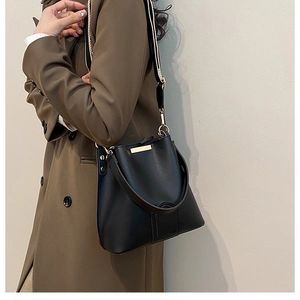 Detail of black leather bucket bag featuring a black and white striped wide shoulder strap