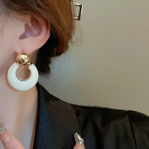 Detailed close-up of a French style gold stud earring with a white enamel hoop drop on a model
