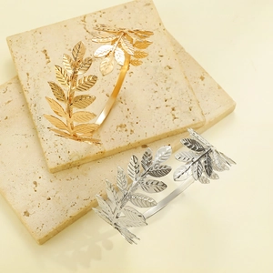 Exaggerated leaf cuff bracelets in gold and silver finish on natural stone background
