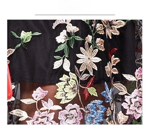 Detailed macro view of colorful floral embroidery on black mesh fabric dress material