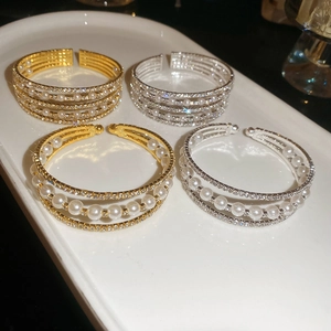 Detailed view of layered pearl and rhinestone open bracelets in gold and silver finish