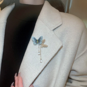 Detail of zircon butterfly brooch with long tassels and crystal teardrop on a beige coat