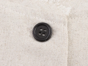 Macro detail of beige textured linen fabric featuring a black button and frayed edge design