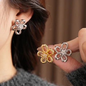 Detailed close-up of hollow flower earrings with zircon centers in gold and silver