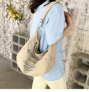 Détail du sac bandoulière en toile montrant la boucle en métal et le lettrage imprimé