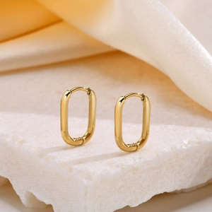Polished gold-tone oval hoop earrings on stone platform with silk background texture