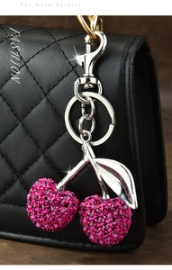 Macro shot of sparkling cherry bag charm with pink rhinestones on a black leather bag