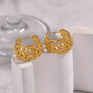 Gros plan de boucles d'oreilles créoles dorées à motif cœur sur socle géométrique blanc