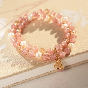 Detail of pink strawberry quartz and pearl bracelet with golden bell on a textured book