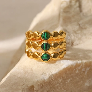 Macro detail of triple-layered 18K gold ring with three green malachite stones on rock