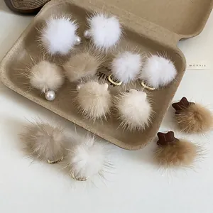 Elegant pearl earrings with plush fur balls in white and brown on a minimalist background