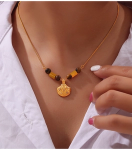 Detail view of gold shell pendant necklace with tiger eye beads on a model