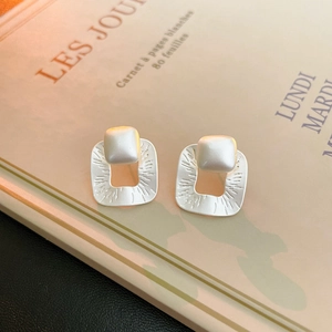 Detailed view of matte geometric square earrings with sunburst texture on a fashion magazine