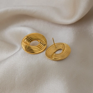 Macro detail of gold oval earrings with textured spiral design on beige silk backdrop