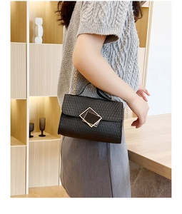 Detalle de bolso bandolera negro con relieve y cierre dorado usado por una modelo