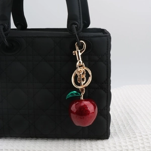 Sparkly red cherry keychain with green leaf and gold clasp on a black quilted handbag