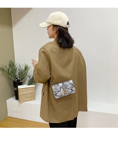 Detail view of snakeskin print small square bag with gold chain strap on a model