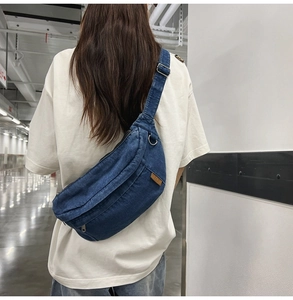 Detail of blue denim crossbody bag featuring a brown leather patch and adjustable strap