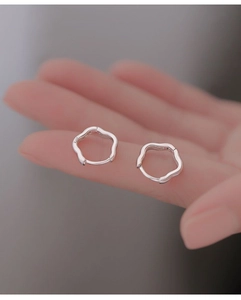 Detailed view of silver wave-shaped hoop earrings on fingers showing S925 sterling silver stamp