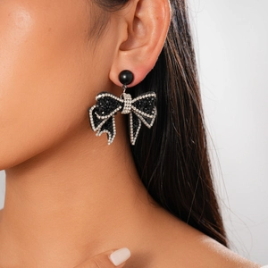 Detailed close-up of dark bow-shaped earrings with rhinestones worn by a model