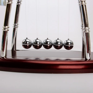 Macro shot of silver metal balls and U-shaped frame on dark red base of Newton's cradle