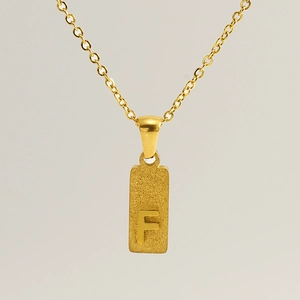 Detailed macro view of rectangular gold pendant with an engraved capital letter F