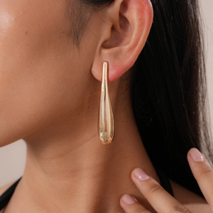 Close-up of a model wearing golden waterdrop earrings with a polished metallic finish