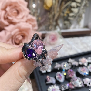 Close-up of pink and purple pear-cut crystals on a dark lava-style ring with nail art