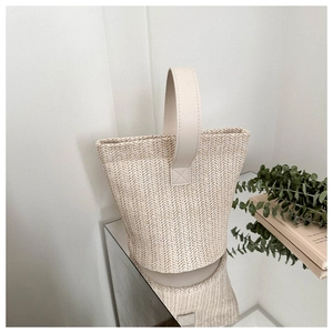 Detail of hand-woven straw bucket bag with premium leather handle and natural fiber texture