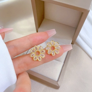 Detail of gold flower earrings with crystals held in hand over a beige jewelry box