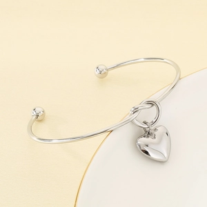Détail du bracelet jonc noué en argent avec un pendentif en forme de cœur sur une surface