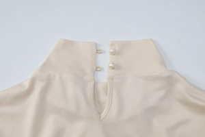 Détail macro du col d'une robe beige avec une élégante fermeture à double bouton perle