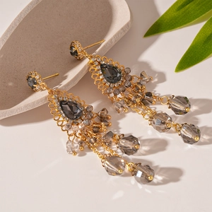 Détail de boucles d'oreilles vintage à pompons dorés et cristaux gris sur plateau
