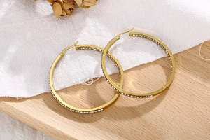 Detailed close-up of gold hoop earrings with white zircon stones on a wooden surface