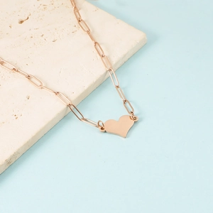 Detail shot of heart pendant on rose gold paperclip chain over textured stone base