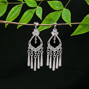 Detailed close-up of ethnic silver tassel earrings with hollow floral design on a branch