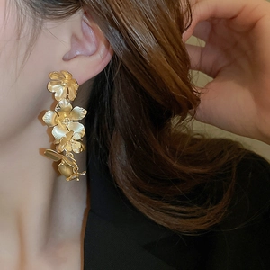 Close-up of golden floral tassel earrings with matte brushed finish on a model