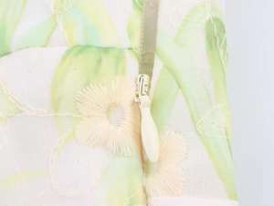Detail of invisible zipper with floral embroidery and leaf prints on cream midi dress