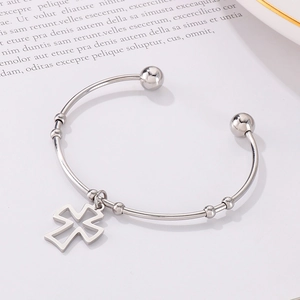 Detailed close-up of a silver open cuff bracelet with a hollow cross charm on book pages