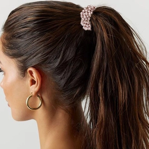 Close-up of pink elastic hair tie with embedded pearls worn on a ponytail by a model