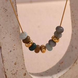 Détail de perles en pierre naturelle colorée et chaîne serpent dorée sur support d'art