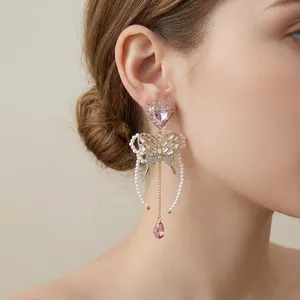 Elegant butterfly and pearl fringe drop earrings with pink heart stones worn by a model