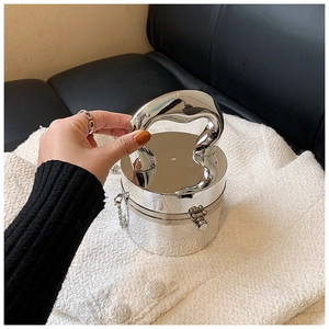 Detail of silver mirror acrylic bag with unique curved handle shown on a black leather sofa