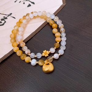Detail of white crystal and gold charm bracelets featuring a lotus and longevity lock pendant