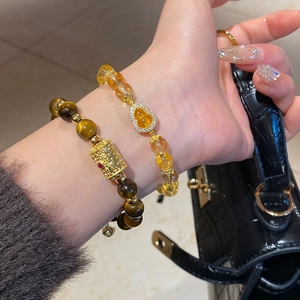 Detail of stacked tiger eye and amber bead bracelets with gold gourd and zircon charms
