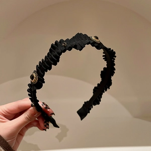 Detail of black pleated fabric headband featuring a gold-edged gemstone decoration