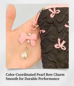 Detail of black quilted cosmetic bag with pink bow pattern and pearl charm accessory